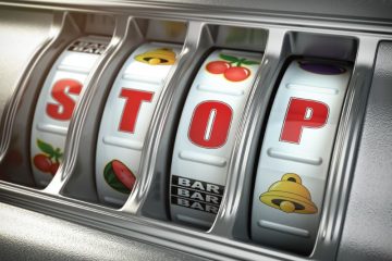 Zbliżenie na automat do gry z czterema bębnami wyświetlającymi symbole owoców i barów. Bębny układają słowo STOP czerwonymi literami na środku, wskazując na konieczność leczenie i skuteczne metody leczenia uzależnienia od hazardu.