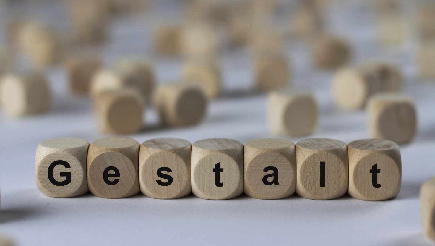 Drewniane klocki z czarnymi literami oznaczają "Gestalt" na pierwszym planie, nawiązując do terapii Gestalt, podczas gdy inne drewniane klocki są rozproszone i nieostre w tle.