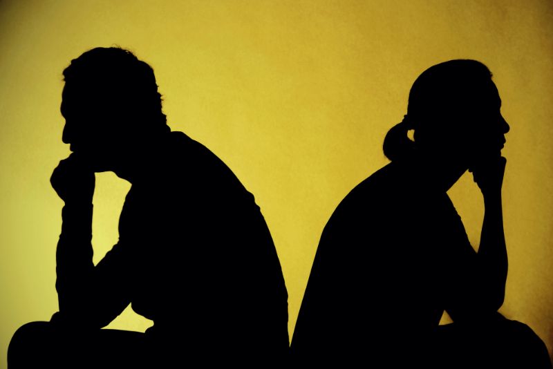 Dwie osoby siedzą tyłem do siebie na żółtym tle, obie wyglądają na zamyślone lub zdenerwowane, a ich dłonie spoczywają na podbródkach - uchwycono objawy złej relacji i napięcie toksycznego związku.