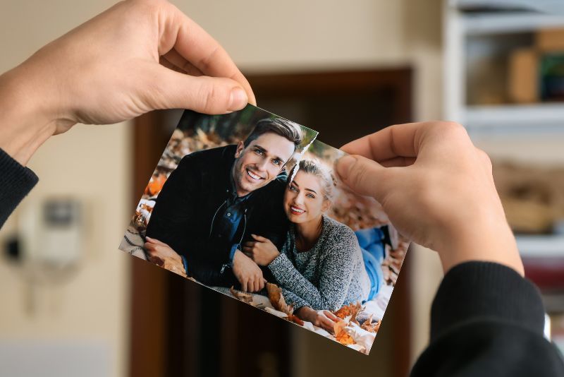 Osoba drze zdjęcie uśmiechniętej pary leżącej na jesiennych liściach, symbolizujące decyzję o zakończeniu związku i ucieczce z toksycznego związku.