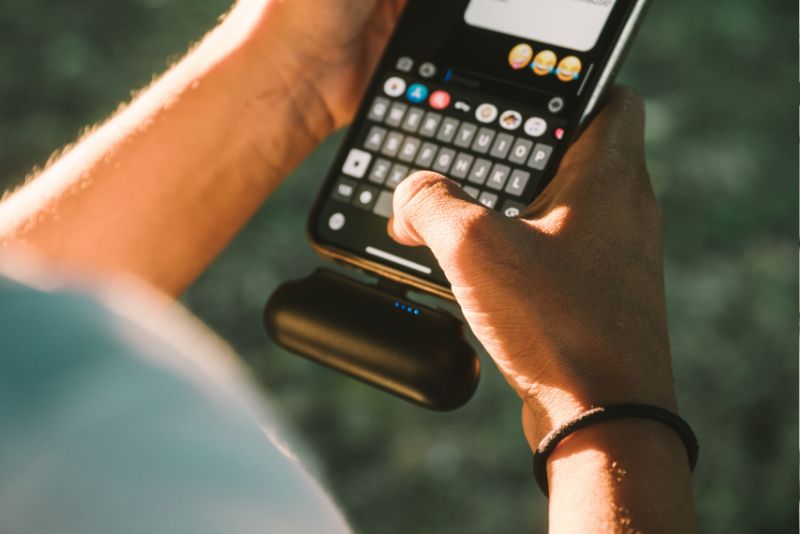 Mężczyzna pisze wiadomość na smartfonie na świeżym powietrzu. Światło słoneczne podkreśla jego dłonie, gdy korzystają z klawiatury aplikacji do przesyłania wiadomości
